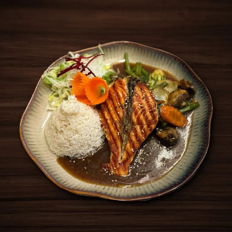 Gegrilltes Lachsfilet mit Sesam auf dunkler Soße, daneben eine Portion Reis, gebratenes Gemüse mit Champignons, grünen Bohnen und Karotte sowie Salat mit Rote-Bete-Streifen.