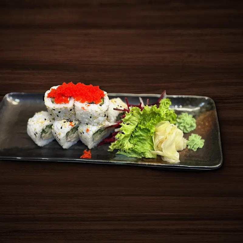 Mehrere Inside-Out-Sushirollen mit Sesam, zwei davon mit orangefarbenem Fischrogen belegt, auf einer schwarzen Platte neben Salat, eingelegtem Ingwer und zwei Tupfen Wasabi.